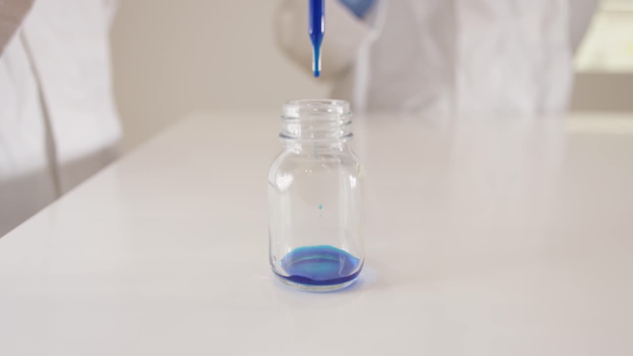 Sample drops of blue ink are poured into a glass by scientists with a pipette in a laboratory