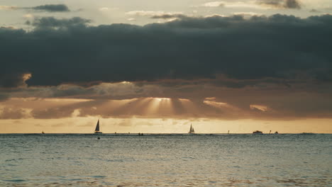 sailboats on the ocean at sunset with sun rays through clouds