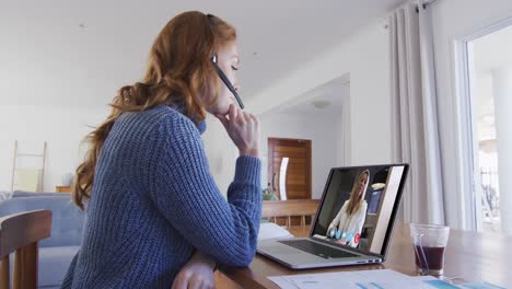 mujer caucásica usando portátil y auriculares de teléfono en videollamada con una colega