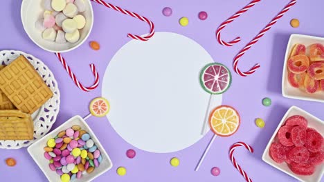 rainbow candies and lollipops appear around paper card note on pastel purple background. stop motion flat lay copy space