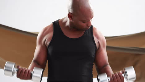 Animation-of-fit-african-american-man-working-out-with-dumbbells-over-blowing-brown-fabric