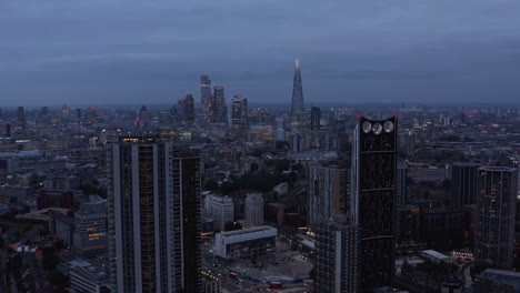 Evening-aerial-footage-of-cityscape.-Tall-residential-buildings-in-Elephant-and-Castle-borough.-Group-of-skyscrapers-in-City-financial-hub-in-background.-London,-UK