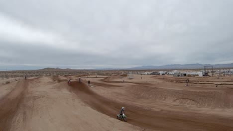 motorcycles taking high jumps as they fly around a racetrack in the mojave desert - leading aerial view