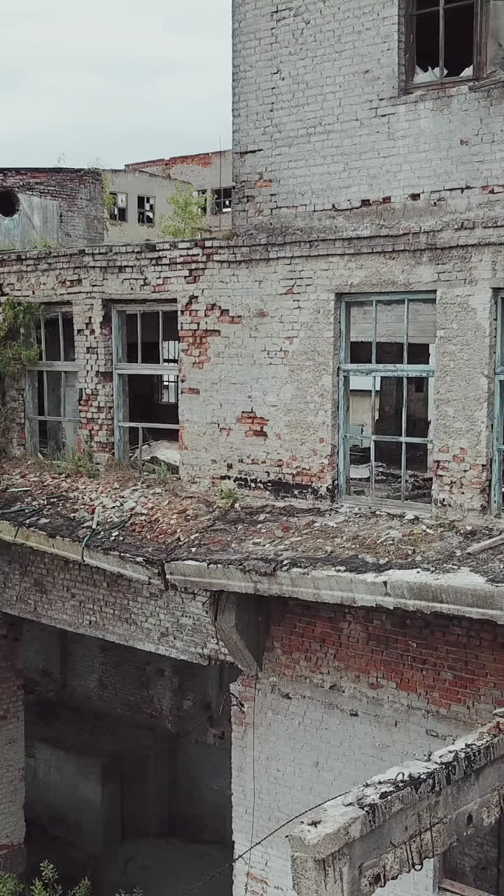 Aerial view of abandoned industrial buildings. Abandoned factory halls with broken glass on windows. Vertical video