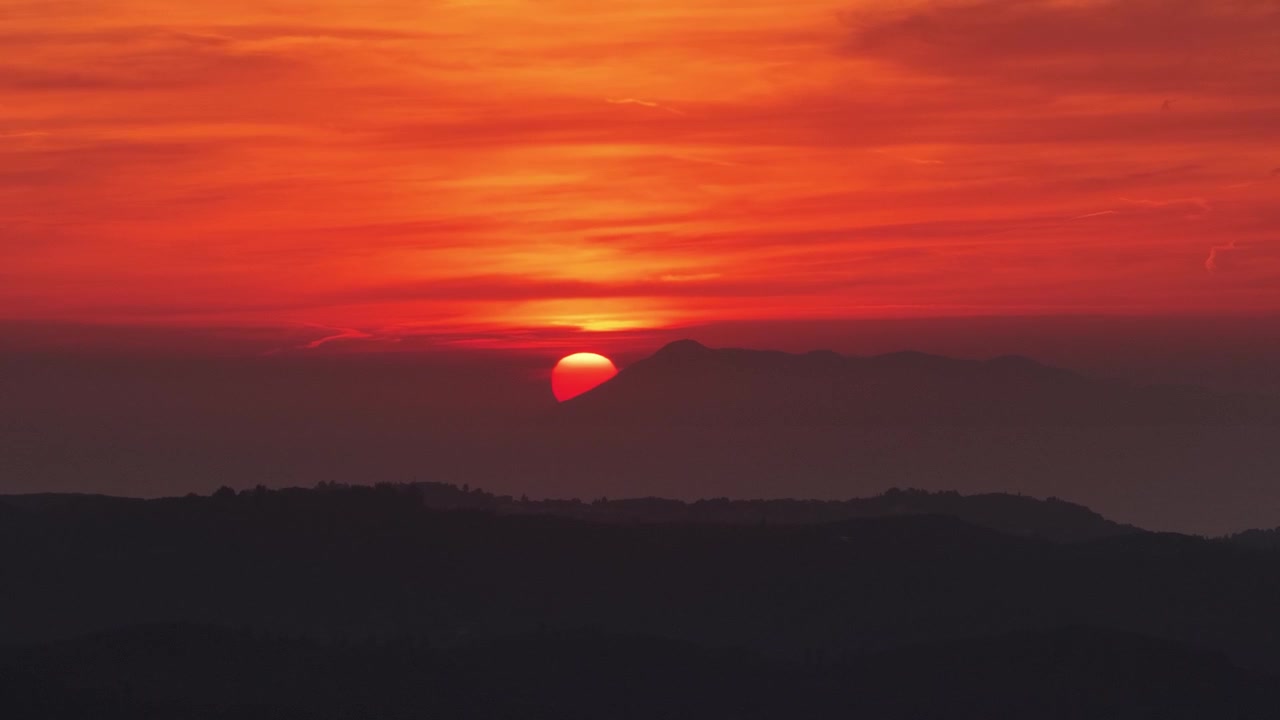 Dramatisk rød solnedgang over bjergtoppe med en glødende sol og silhuetlandskab i Agioi Douloi, Nordkorfu, Grækenland