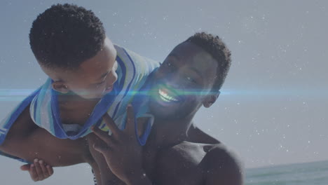 animation of light trails over african american man and his son playing together at beach