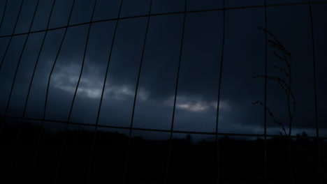 looking through metal fence into dark evening sky, nightfall with moving clouds, rural scene