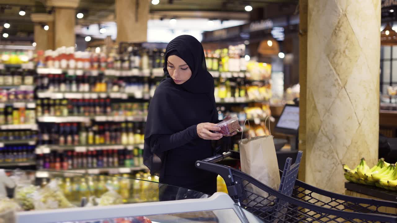 mujer musulmana comprando comestibles, tomando algunas bayas del pasillo de frutas