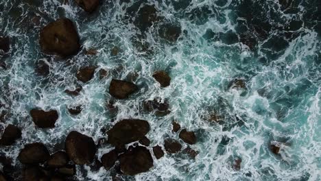 Aerial-top-view-foamy-waves-break-on-dark-rocks-near-beach.-Sea-waves-on-the-dangerous-stones-aerial-view-drone-4k-shot.-Bird's