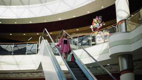 beautiful lady wearing black crop top under pink dress descending an escalator holding shopping bags in her left hand while her right hand is on the rail, toys and other items are visible upstairs