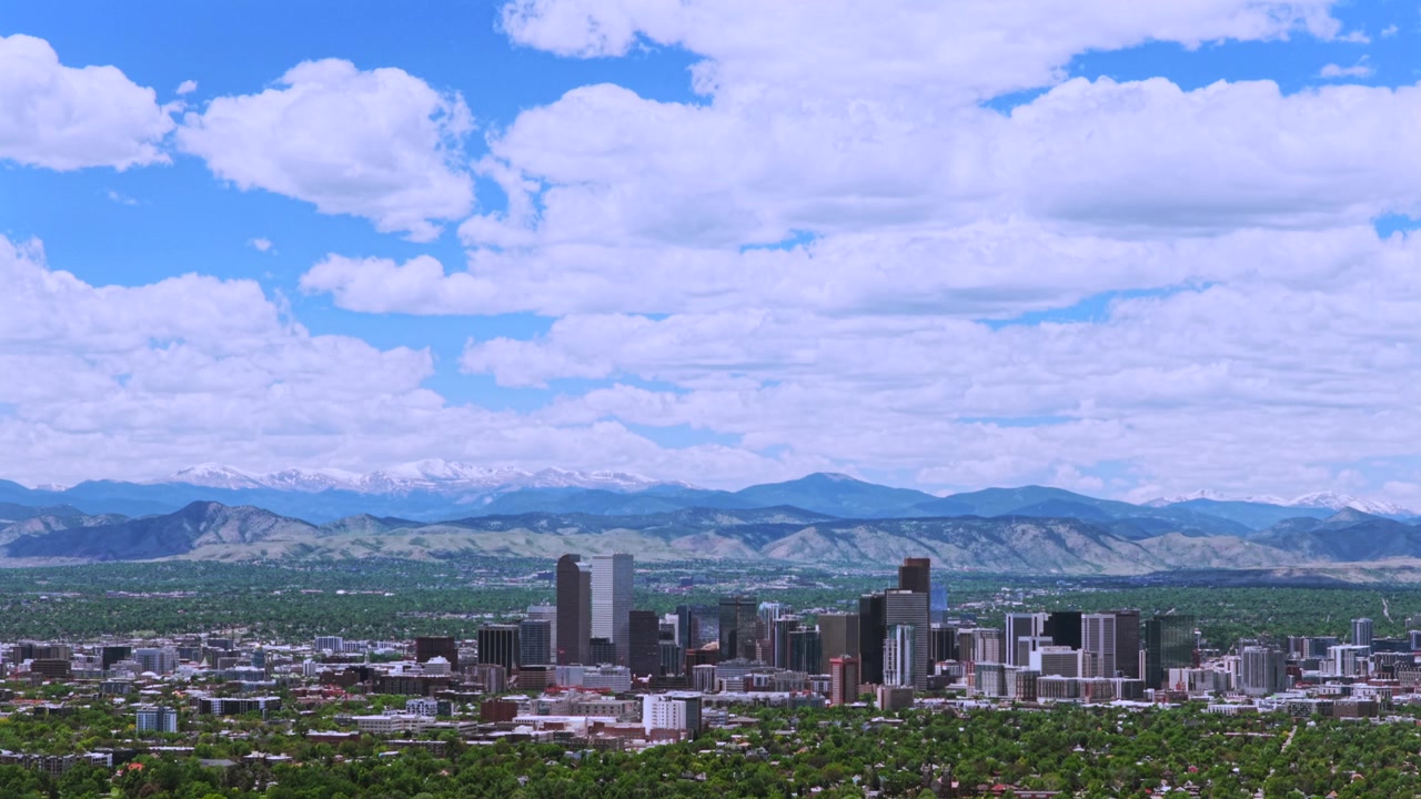 Denver by, Front Range. Bybillede med skyskrabere og bygninger, landskab ved foden af bjergene, downtown Denver, Colorado. Droneoptagelse om foråret af kvarterer om morgenen med blå himmel, skyer og sneklædte Rocky Mountains, set opad.