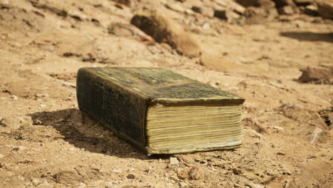 ancient book resting on dry soil in an outdoor setting during daylight