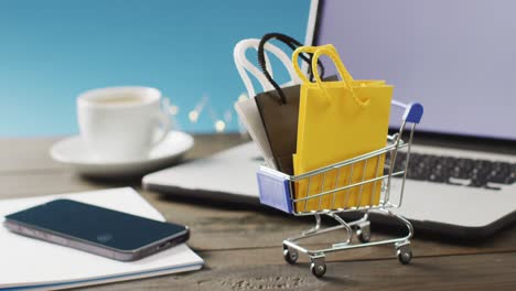 gift bags in shopping trolley on desk with smartphone and laptop