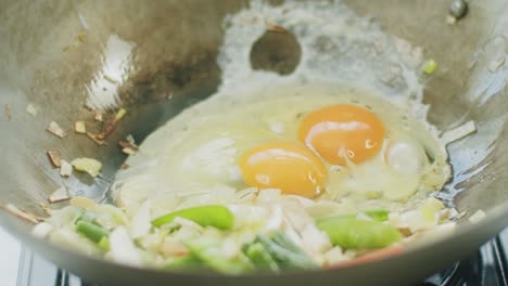 person mixing eggs in pan with frying vegetables