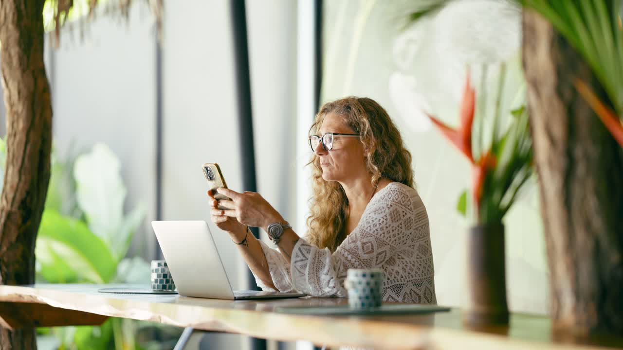 Donna che lavora da remoto con telefono e laptop in un caffè