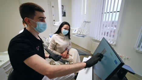 Male dentist is showing the denture projection on the screen. Touch screen picture is rotated by the doctor to demonstrate it to the patient and discuss problems and ways of their solving.