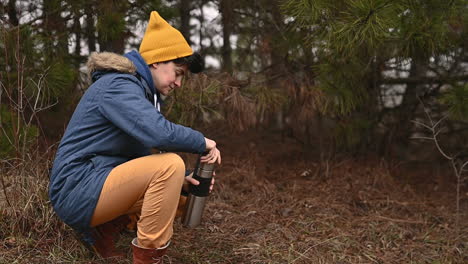 A-Young-Female-With-Short-Hair-Opens-Her-Hot-Water-Thermos-In-The-Forest