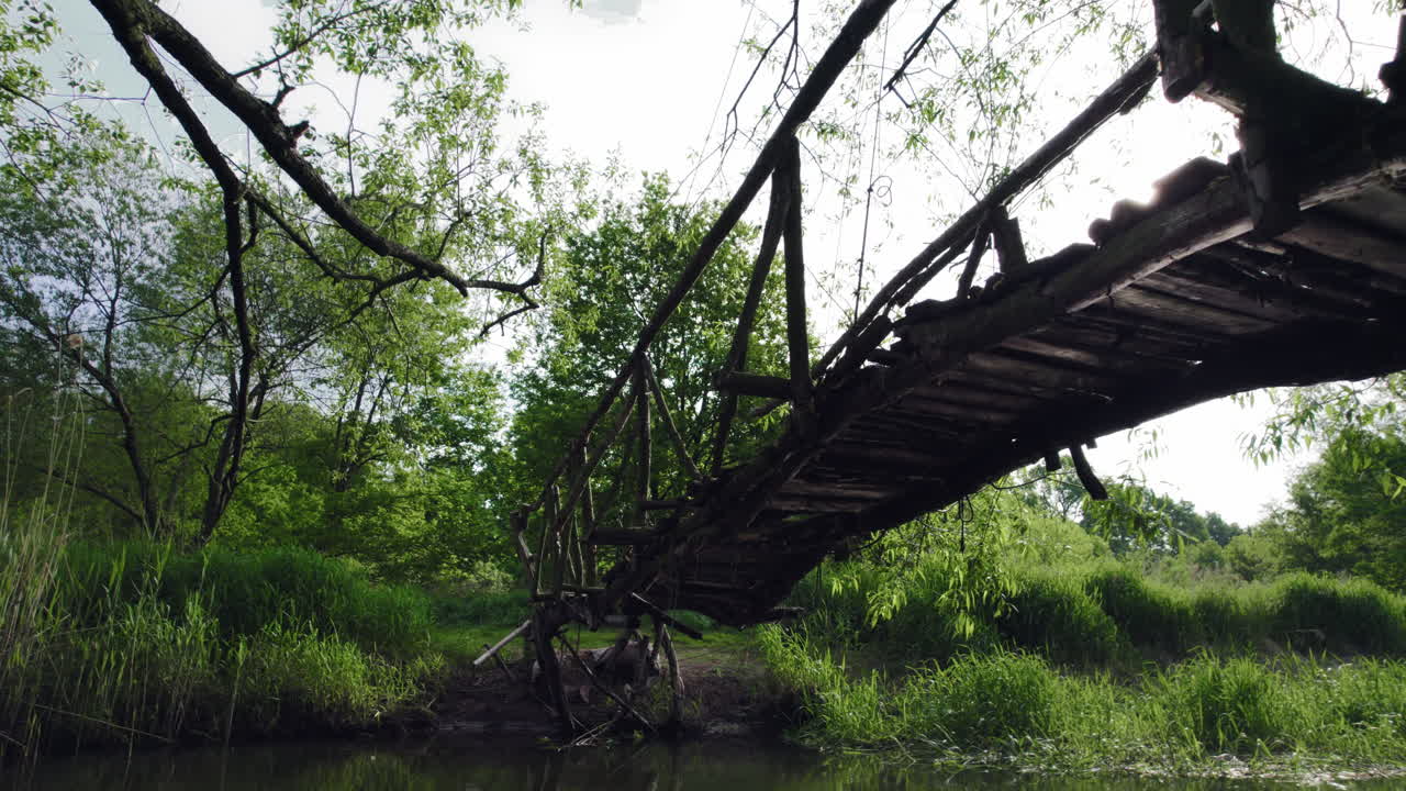 bottom of handmade wooden bridge over a small river in forest with water waves reflecting and sun rays shining between planks