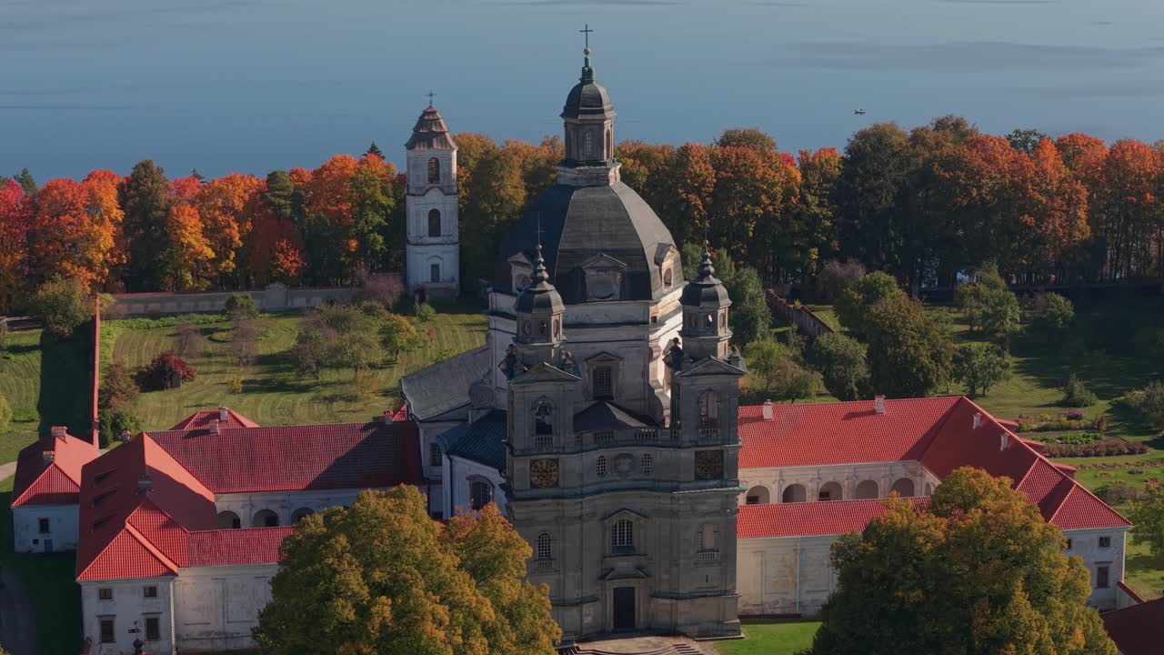 Close-up aerial view of Pažaislis Monastery in Kaunas, Lithuania, with vivid autumn trees and Kaunas Reservoir in the background. Historic Baroque church surrounded by nature