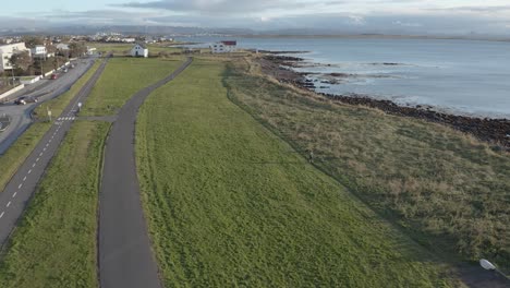 Person-running-on-nature-trail-along-coast-at-Reykjavik-during-sunset,-aerial