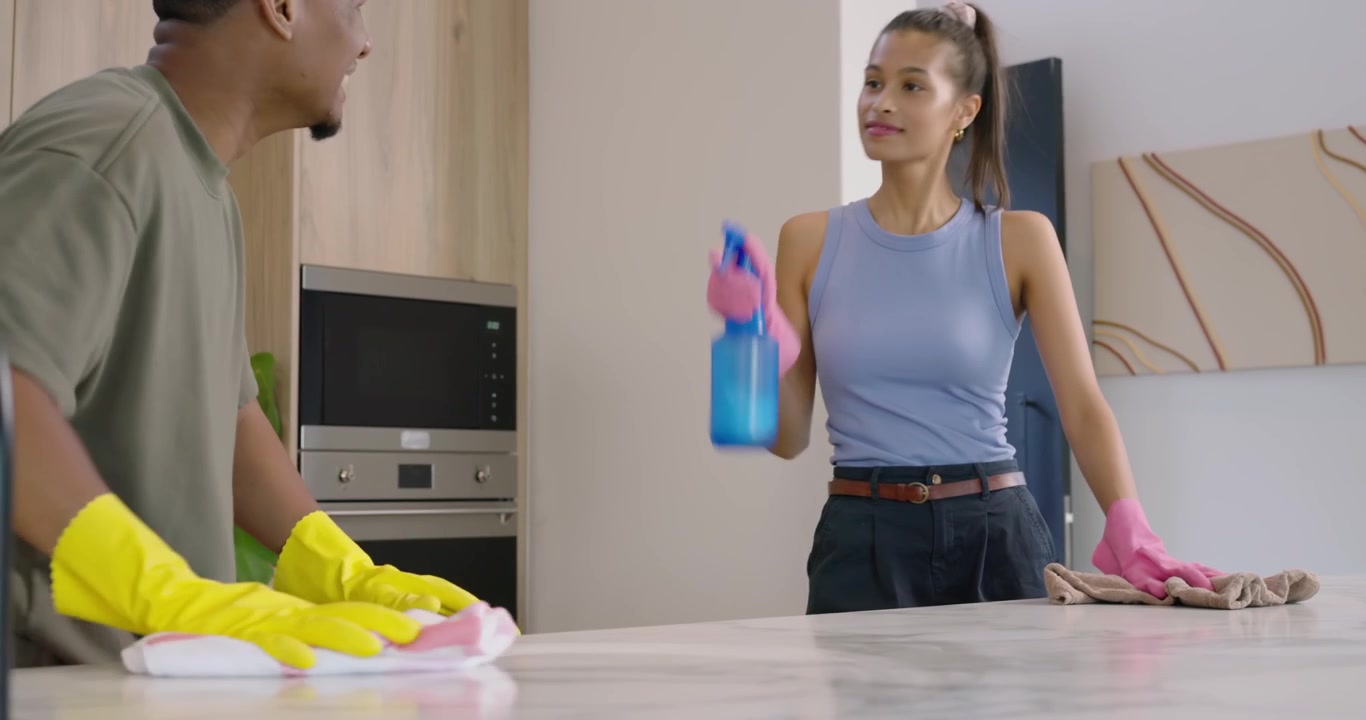 African American couple seeing mess spraying wiping kitchen island with blue bottle wearing gloves