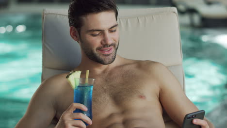 closeup sexy man relaxing with phone by pool. cheerful man scrolling mobile