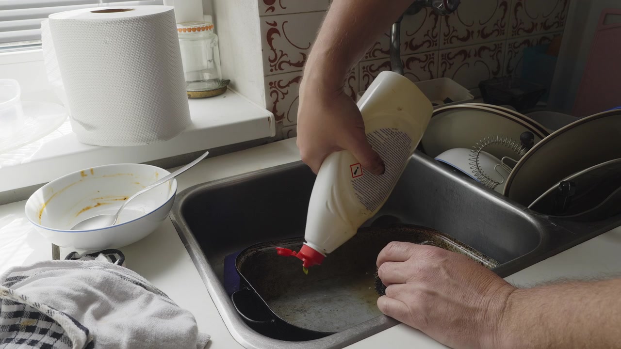 Il detersivo liquido viene utilizzato per affrontare i residui incrostati durante una pulizia approfondita della cucina. Una scena domestica riconoscibile che evidenzia la pulizia, la cura della casa e le faccende domestiche quotidiane.