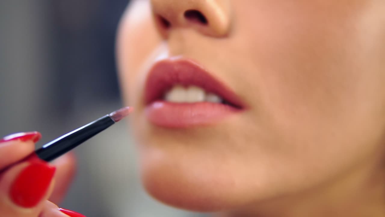 Close Up view of a professional makeup artist applying lipstick on model's lips working in beauty fashion industry. Close Up view