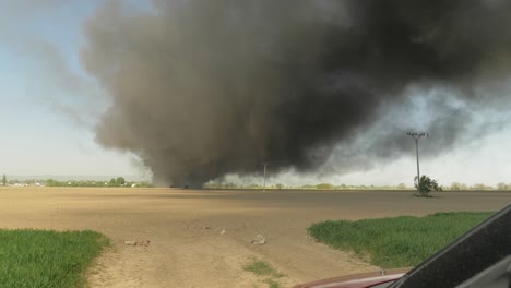 view from car facing black smoke from farm crop fire, rising shot