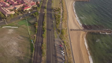 drone aerial view of road, beach and railway line at st kilda beach, panning upwards, day time sunset, australia melbourne