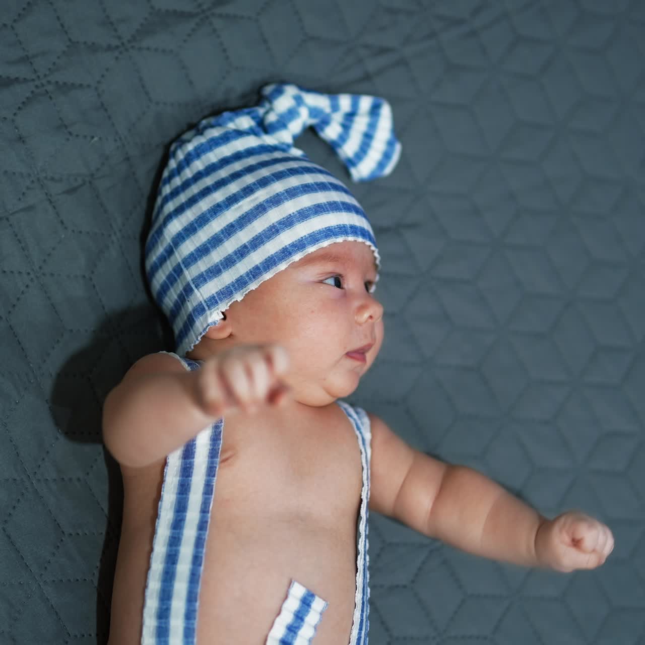 Funny beautiful infant lies on the bed and turns away his head from the camera. Baby on the grey background. View from above