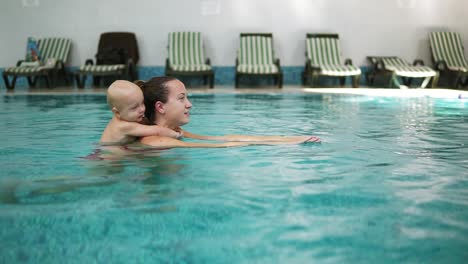 Die-Junge-Mutter-Schwimmt-Im-Pool-Und-Hält-Ihr-Kleines-Süßes-Kleinkind-Auf-Dem-Rücken