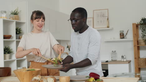 wife putting salad on plate for husband in kitchen