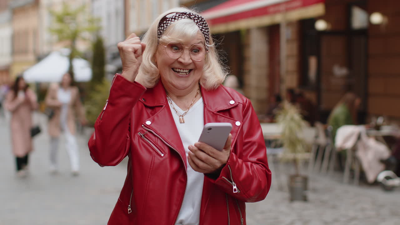 Una donna anziana usa uno smartphone mobile per festeggiare la vittoria con un buon messaggio di notizie all'aperto in una strada della città urbana