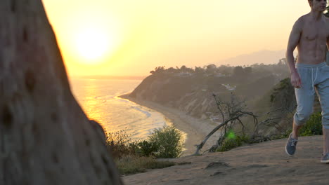 Young-fit-shirtless-man-watching-a-golden-sunset-after-a-workout-and-run-on-the-edge-of-a-cliff-above-the-Pacific-ocean-in-Santa-Barbara,-California