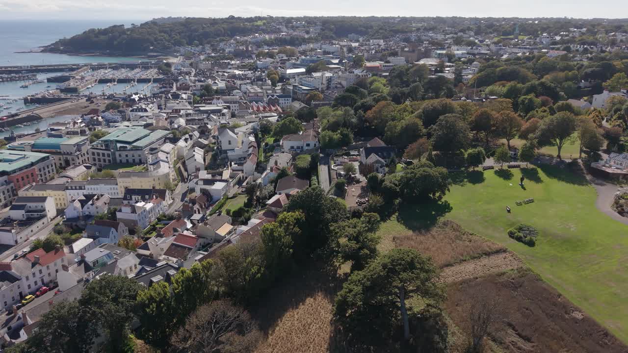 High forward drone footage over Les Cotils Christian Centre St Peter Port Guernsey and onwards above the roof tops of the town on bright but cloudy day with town the harbour and Havelet Bay