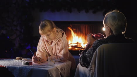 randmother with a little girl on christmas eve have a rest by the fireplace the girl writes a letter