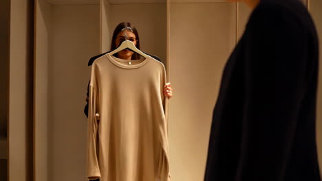woman trying on a beige shirt or dress in front of a mirror