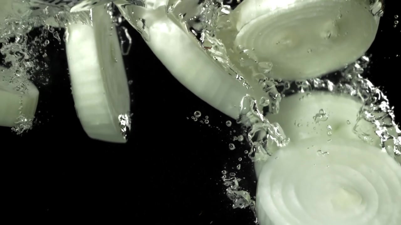 White Onion Slices Falling into Water with Bubbles on Black Background