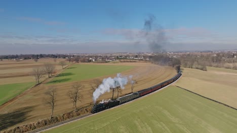 An-Aerial-View-in-Slow-Motion,-of-a-Steam-Passenger-Train-Approaching,-Around-a-Curve,-Blowing-Smoke,-while-Traveling-Thru-the-Countryside,-on-a-Sunny-Winter-Day,-on-a-Sunny-Winter-Day