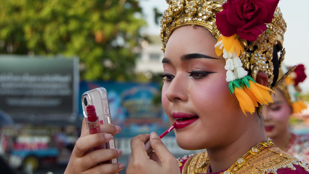 Thai Dancer Applying Lipstick While Looking at Smartphone