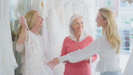 sales assistant with adult daughter helping mother to choose wedding dress in bridal store