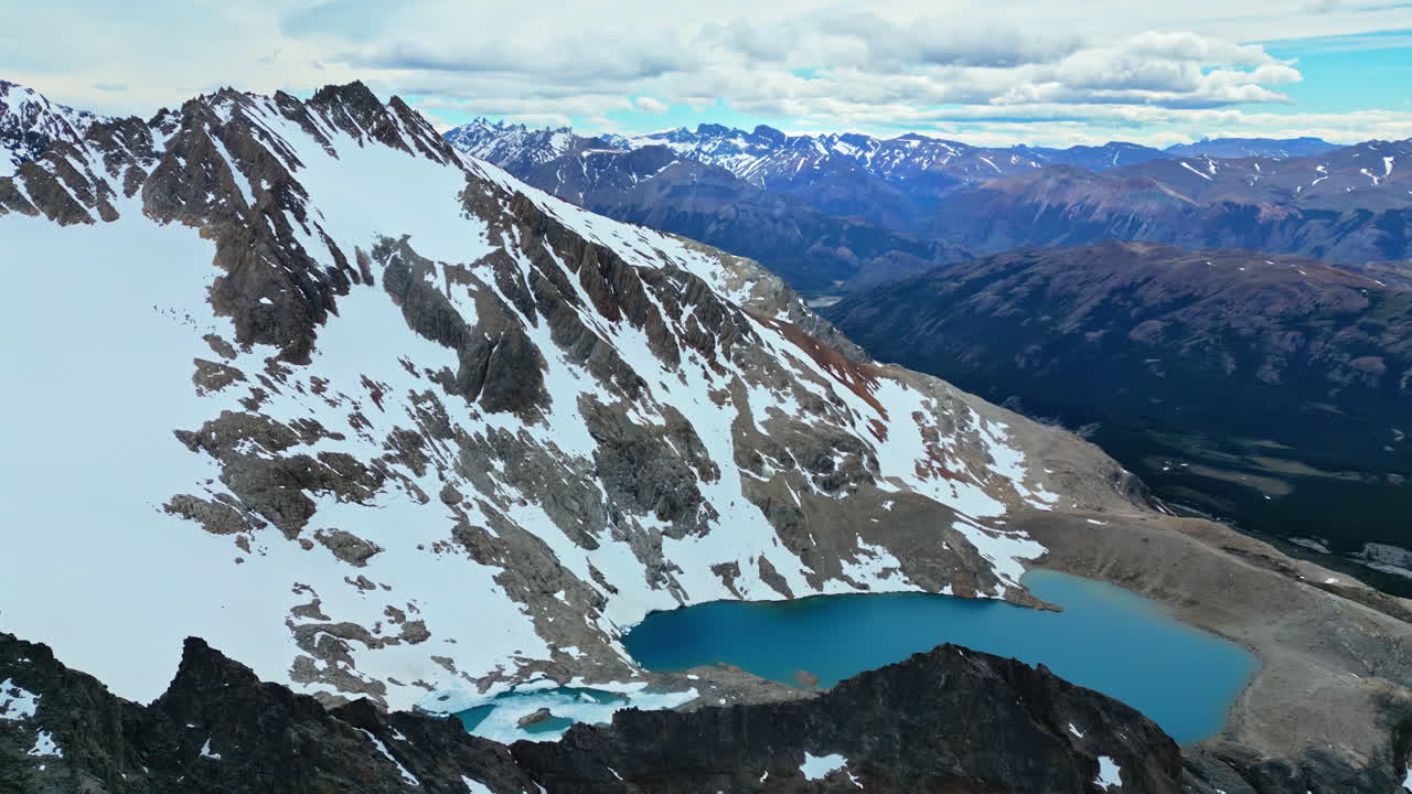 Aerial drone view of a bright turquoise glacial lake nestled between steep rocky cliffs and snow covered peaks