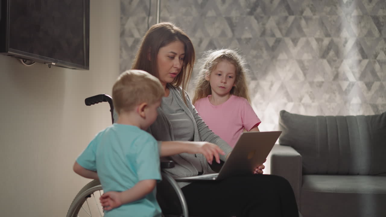 la madre muestra imágenes de los niños en la computadora portátil sentada en silla de ruedas