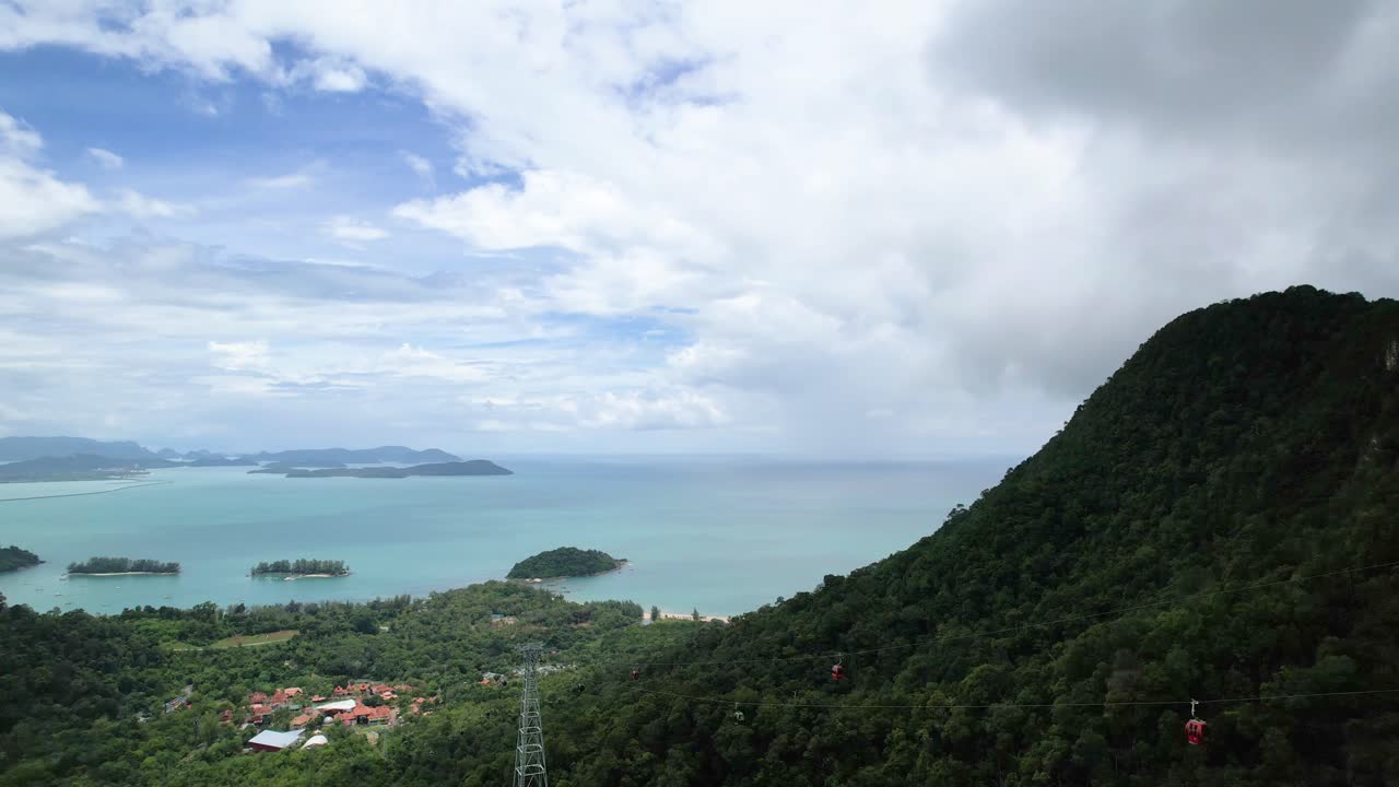 Malezya'daki Langkawi Adası'nda yemyeşil dağlar üzerinde hareket eden teleferik manzarasına sahip sakin mavi okyanus panoraması.