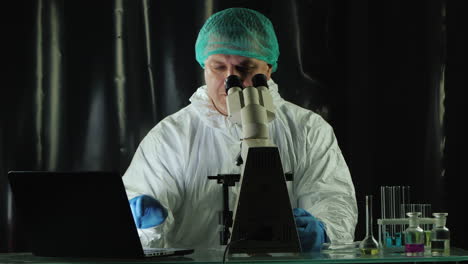 researcher in viral lab works with microscope and laptop