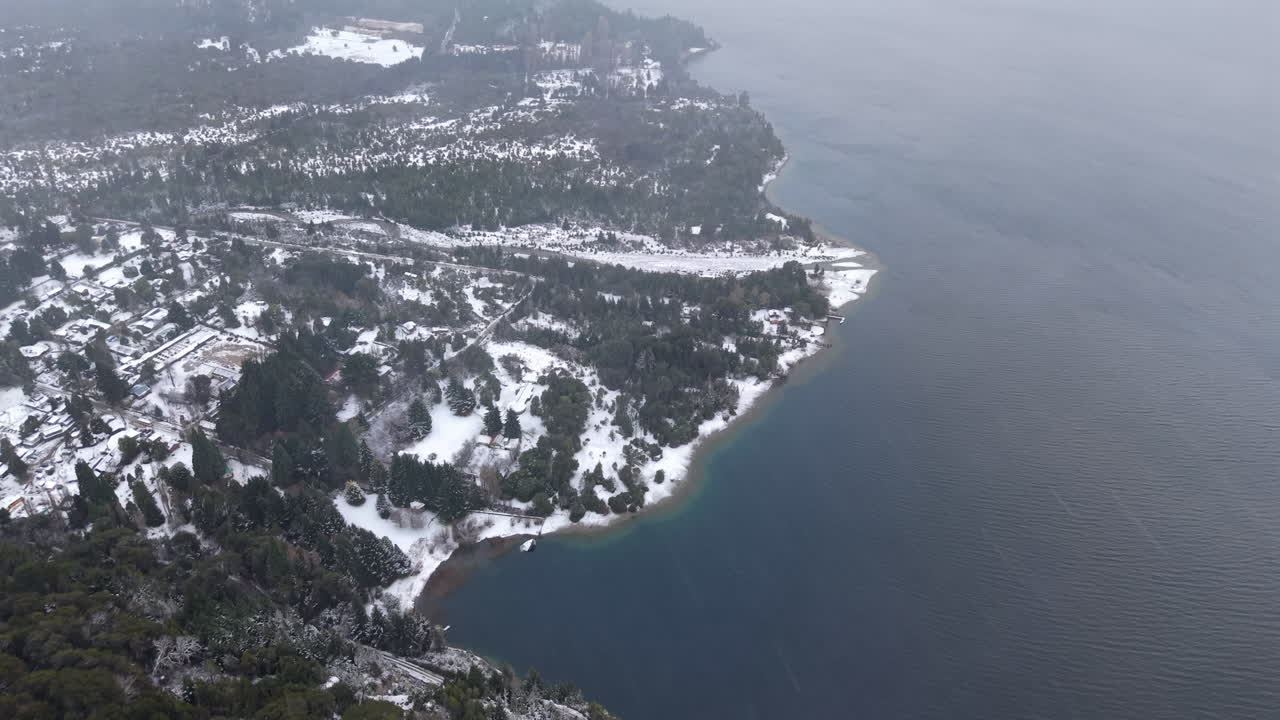 Aerial winter view of snowy shoreline where forest meeting beautiful lakeside landscape at Colonia Suiza, Bariloche, Argentina