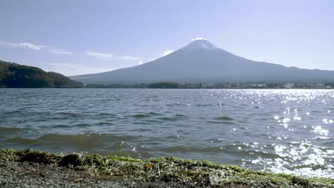 vista de ángulo bajo del monte fuji en la distancia con el lago y pequeñas olas rompiendo en la playa