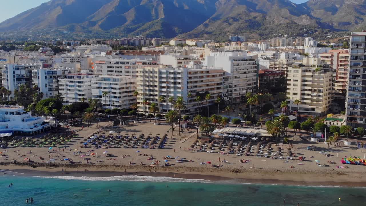 drone disparado retrocediendo sobre el mar desde la playa y la ciudad de marbella, españa