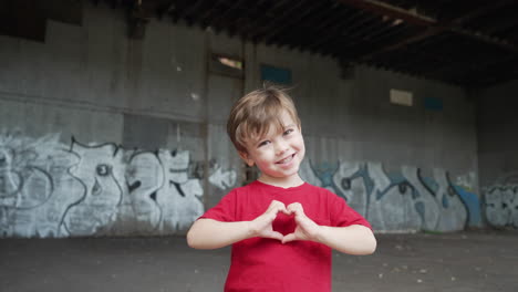un niño pequeño se está divirtiendo y haciendo símbolos de corazón con las manos frente a la cámara en una camiseta roja